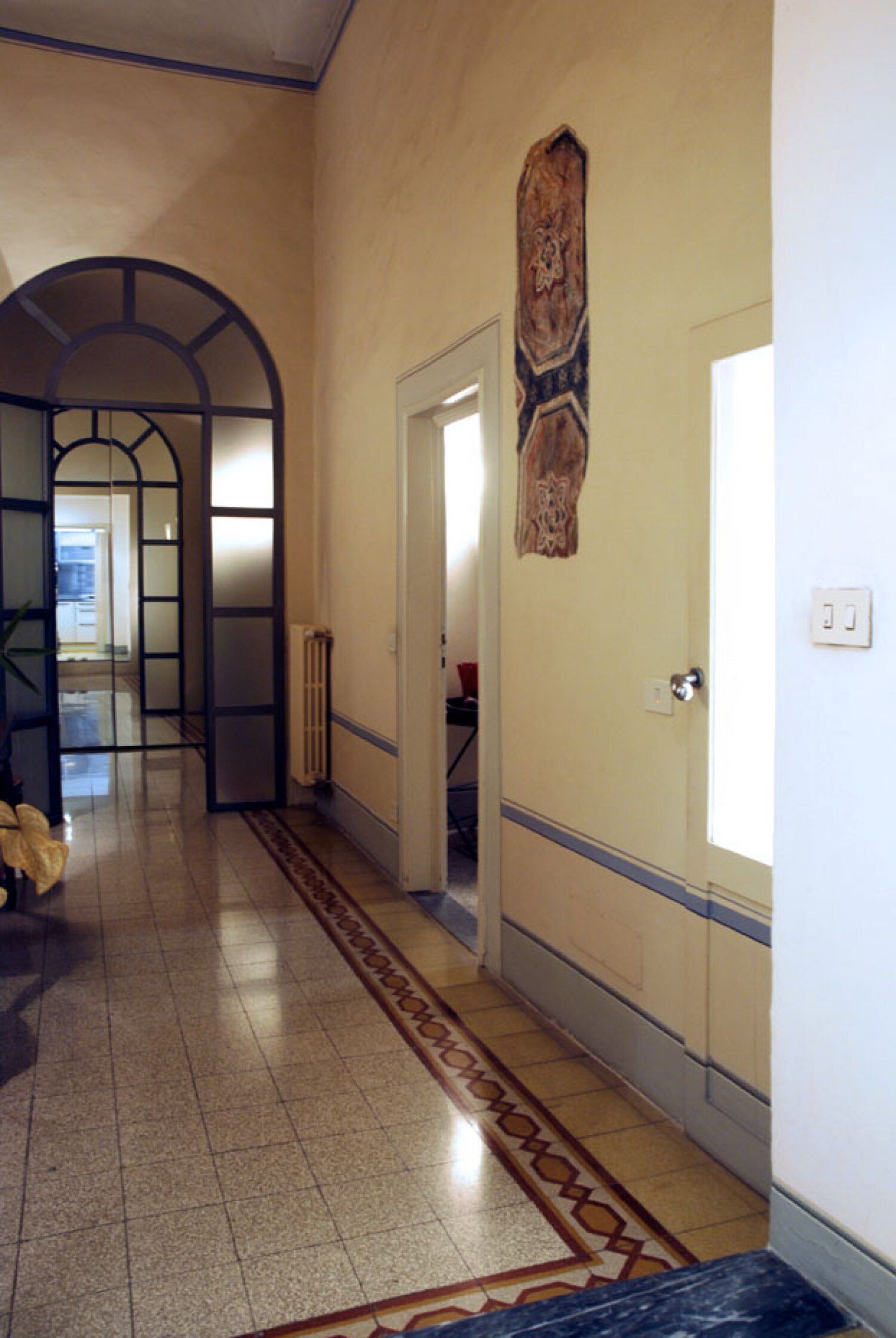 A hallway with a tiled floor, a door with a decorative panel, and a radiator.