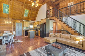 Un vaste espace de vie doté d’un plafond haut, d’un décor intérieur en bois, d’un îlot central et d’un escalier avec une rampe en métal.