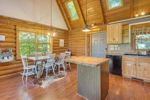 L’intérieur d’une cabane en rondins comprend un coin repas, une cuisine et de grandes fenêtres.