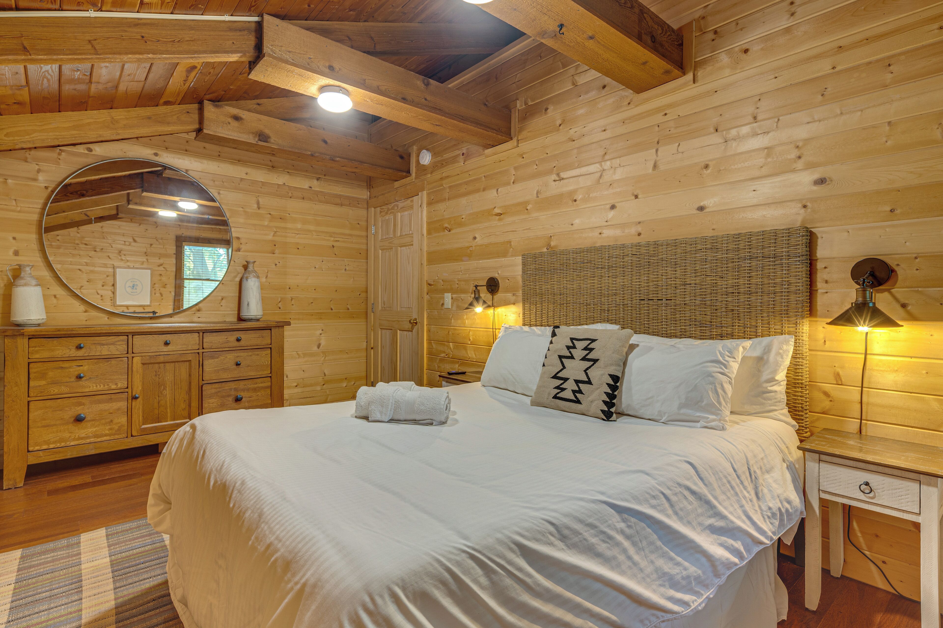 A wooden cabin-style room with a bed, a dresser, a mirror, and a lamp.