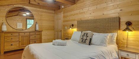 A wooden cabin-style room with a bed, a dresser, a mirror, and a lamp.