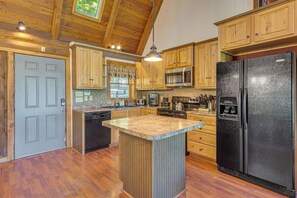 Cucina con mobili in legno, frigorifero nero, microonde e isola con piano di lavoro in granito.