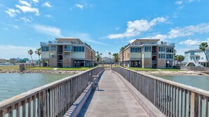 A waterfront property with a long pier leading to a building with balconies and a view of the water. - This fabulous upscale condo, complete with elevator access, sits right on the sh (Port Aransas)
