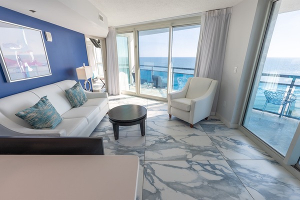 - Bright living room with oceanfront balcony views through floor-to-ceiling glass doors - Comfortable seating with modern coastal decor and accent wall for a relaxing stay - Spacious layout with natural light perfect for a Myrtle Beach vacation rental