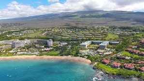 Un resort costero con varias construcciones, una playa y montañas al fondo.