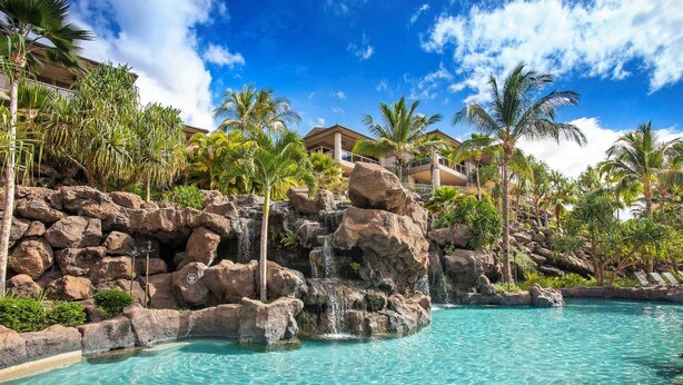 Una piscina con agua turquesa cristalina, rodeada de rocas grandes y palmeras.