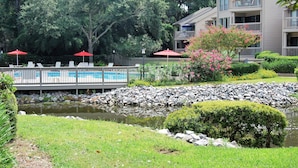 A pool area with lounge chairs and umbrellas, surrounded by a stone wall and greenery.