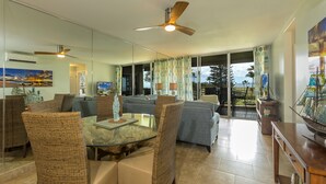 A spacious living area with wicker furniture, a glass dining table, and a ceiling fan.