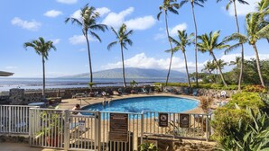 A private pool with a view of the ocean and a mountain, surrounded by palm trees and a white fence.