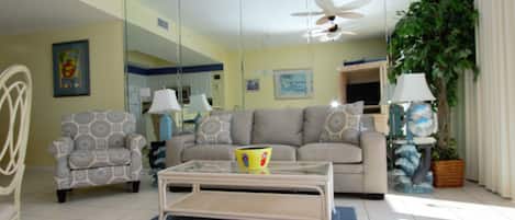 Relax in this stylish living room with a beige sofa, armchair, and coffee table, complemented by a large mirror and a potted plant.