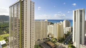 A high-rise building with a view of the ocean and a green park area.