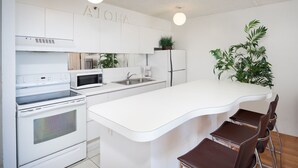 A modern kitchen with white appliances, a central island, and a seating area with brown chairs.