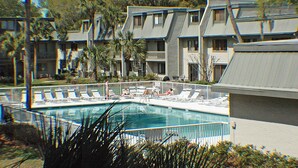 Una piscina rodeada de sillas de descanso y palmeras, con un edificio de varios pisos al fondo.