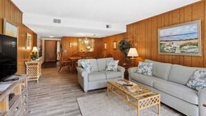 Una sala de estar con un sofá, televisión, mesa de comedor con sillas y paneles de madera en las paredes.