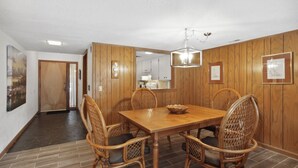 Un comedor con una mesa y sillas de madera, una araña y paneles de madera en las paredes.