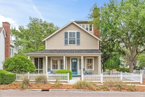 A two-story house with a front porch, a blue door, and a white picket fence.