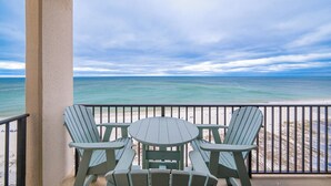 Ein Balkon mit zwei Adirondack-Stühlen und einem kleinen Tisch, mit Blick auf einen Strand und klare Sicht auf den Ozean.