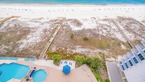 Blick auf einen Strand mit Poolbereich, einem Rettungsschwimmturm und einer Promenade, die zum Strand führt.