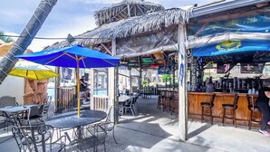Un área de bar al aire libre con sombrillas de estilo tiki, sillas de metal y una barra.
