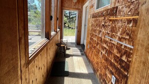 A narrow wooden hallway with a bench, a fan, and a door leading outside. - Surfrider - Cozy Beach Cabin, Close to Beach, Pool Table (Pacific City)