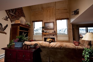 A cozy living room with a fireplace, wooden walls, and a view of snow-capped mountains. - Cascade Village Condo - Awesome Views - Heated Pool (Durango)