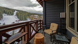 A balcony with a view of a snowy mountain and a building. There are wooden benches and a chair. - Steps to American Flyer lift & Stellar Mtn Views! Hot Tub, Free Wifi, Heated Pkg (Copper Mountain)