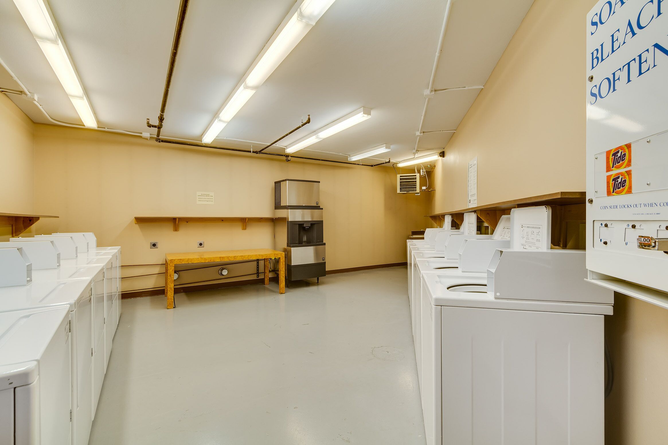 A laundry facility with multiple washing machines, a bench, and a water heater.
