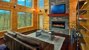 Ein geräumiges Wohnzimmer mit Kamin aus Stein, einer Ledersofa und einem flachbildfernseher, der darüber angebracht ist.