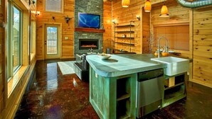 Eine moderne Küche mit Kamin aus Stein, Holzwänden und einer großen Kochinsel mit Spüle und Geschirrspüler.