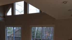 Un vaste salon doté d’un plancher en bois, d’une table basse sombre et d’un canapé marron. De grandes fenêtres offrent une vue sur une terrasse en bois et sur les arbres.