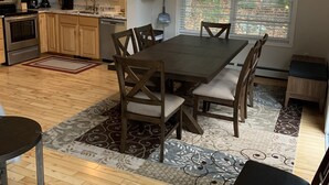 Une cuisine spacieuse avec des meubles en bois, une table à manger avec des chaises et une grande fenêtre donnant sur les arbres.