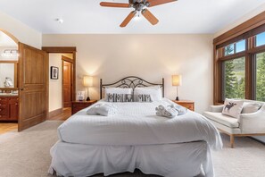 Une chambre à coucher avec un grand lit, des lampes de chevet, un ventilateur de plafond et une vue sur l’extérieur par une fenêtre.