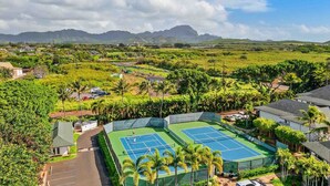 A tennis court surrounded by lush greenery and residential buildings.