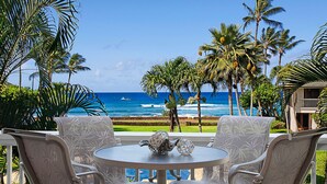 Un patio con una mesa redonda y sillas, con vista a una playa con palmeras y al océano.