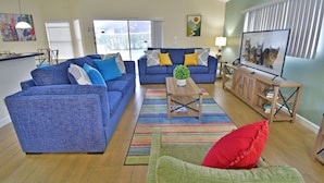 A living room with two blue sofas, a green armchair, a wooden coffee table, and a TV on a stand. - Home in Peaceful Community With Pool, Spa & Privacy Hedges (Davenport)