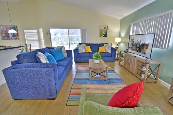 A living room with two blue sofas, a green armchair, a wooden coffee table, and a TV on a stand.