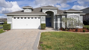 A residential house with a white garage, a covered entryway, and a landscaped front yard. - Home in Peaceful Community With Pool, Spa & Privacy Hedges (Davenport)