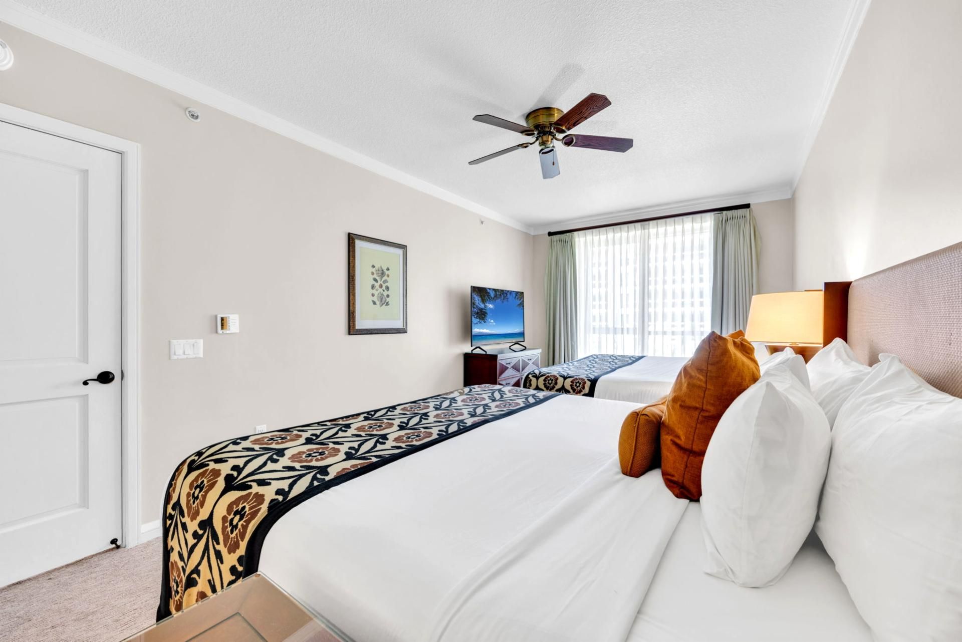 Quarto de hotel com cama, ventoinha no teto, televisão e janela com cortinas.