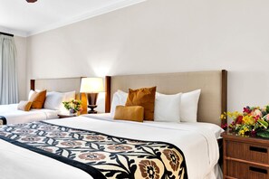 Une chambre d’hôtel avec deux lits, une table de chevet avec une lampe, un vase décoratif et une petite table en bois sur laquelle est posé un autre vase rempli de fleurs.
