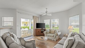 Un salon moderne comprenant un canapé, une table basse, un meuble pour la télévision et un ventilateur de plafond.