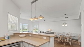 Une cuisine dotée d’un îlot central, de meubles blancs et d’un coin repas avec des chaises et une table en osier.