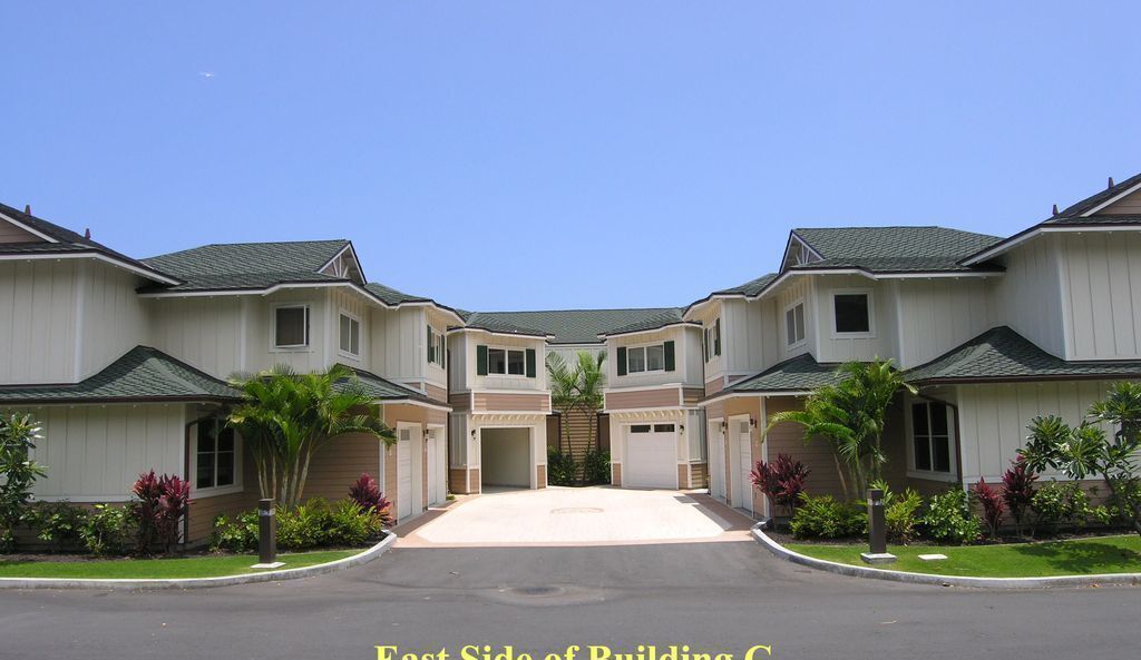 A row of two-story houses with a central driveway, each with a garage and surrounded by small trees and shrubs.