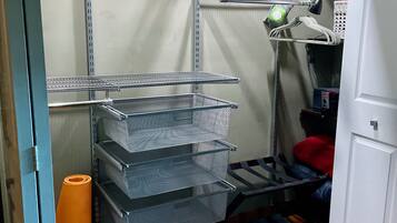 Un espace de rangement équipé d’étagères métalliques, de paniers et d’un tapis enroulé.