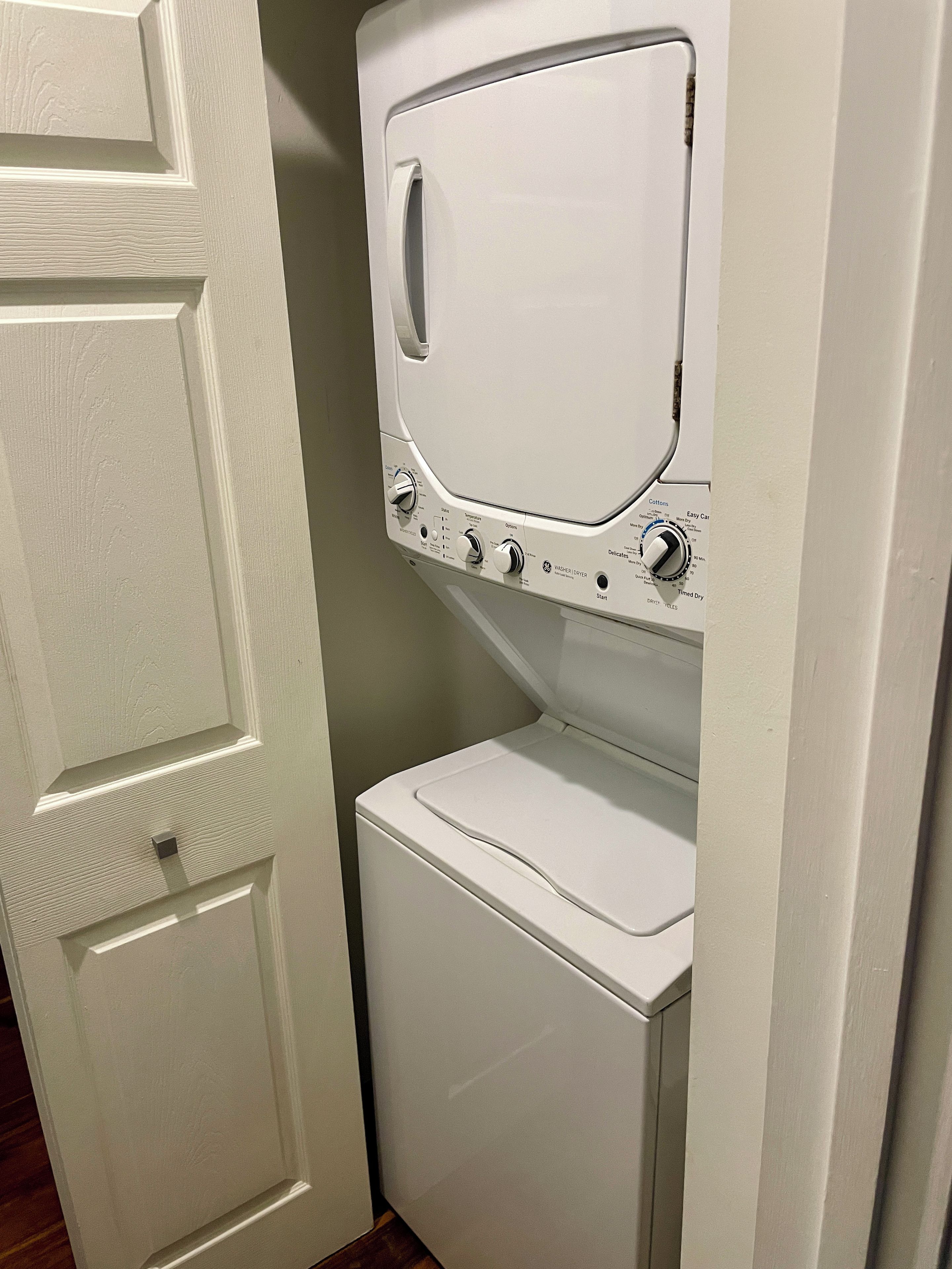 Een compact wit was- en droogcombinatie, bevestigd aan de muur, met bedieningsknoppen en een voorpaneeldeurtje.