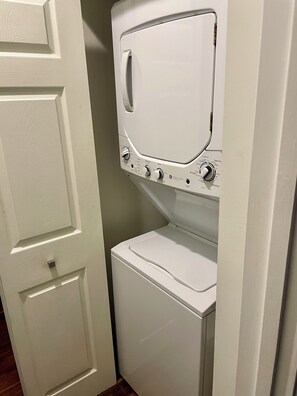 Un appareil compact, blanc, comprenant une machine à laver et un sèche-linge, conçu pour être fixé au mur, avec des boutons de commande et une porte à l’avant.