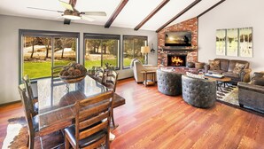 A spacious living area with a fireplace, large windows, and a dining table with chairs.