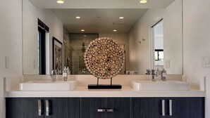 A modern bathroom with two sinks, a large mirror, and a unique wooden sculpture centerpiece.