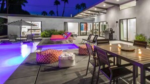 A modern outdoor living area with a pool, lounge chairs, and a dining table with candles.