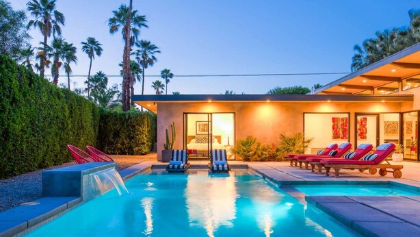 A modern pool area with lounge chairs, a small waterfall feature, and a building with artwork.