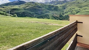 Un banc donnant sur un champ verdoyant, avec une chaîne de montagnes en arrière-plan et un téléphérique.